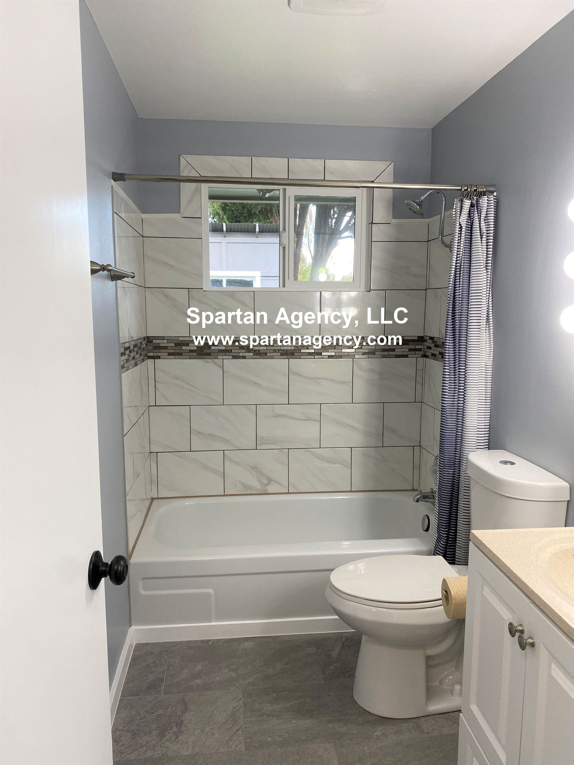 Bathroom with white and gray tiled walls and a shower curtain. Features a toilet, vanity, and bathtub.