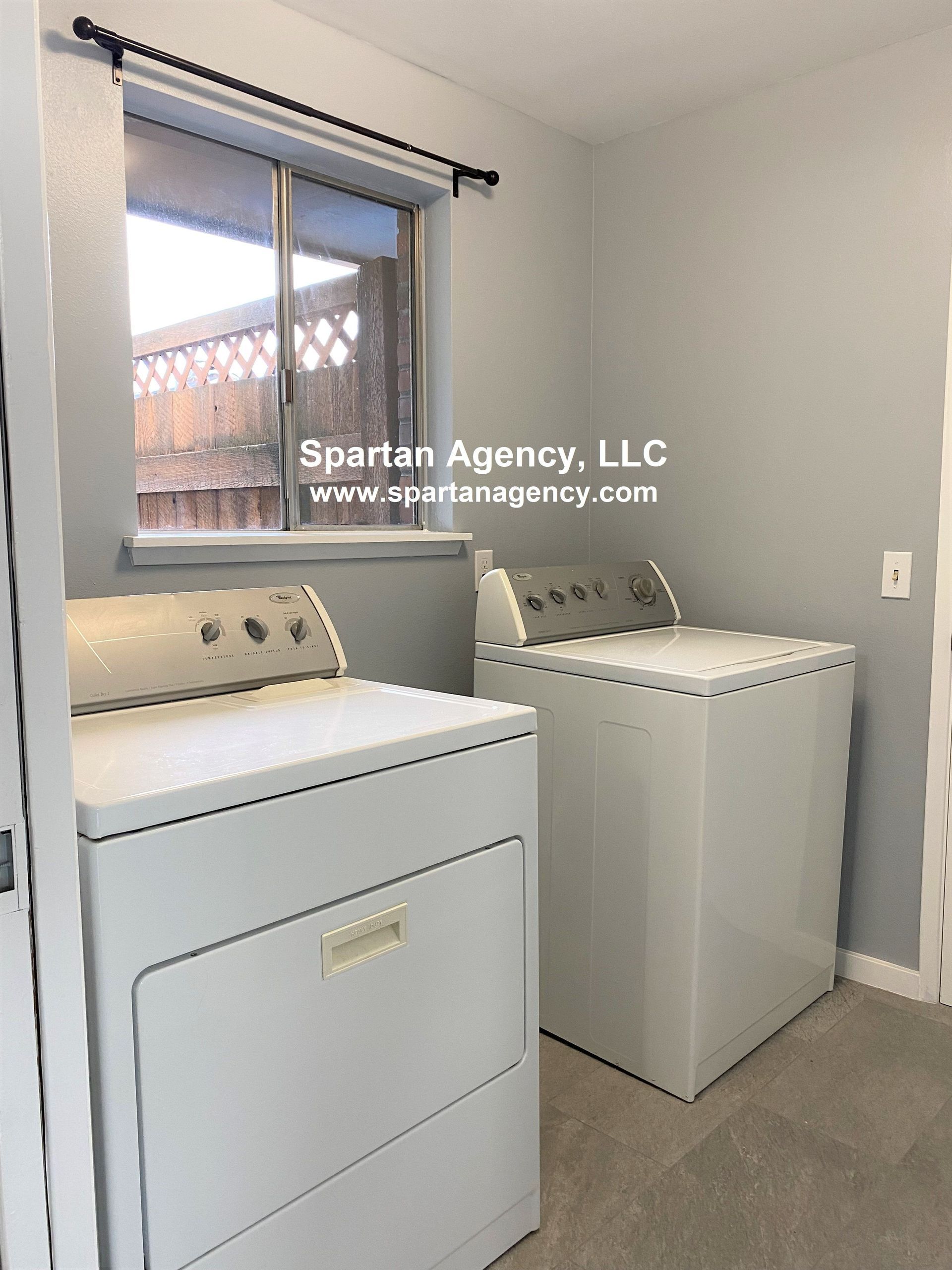 A laundry room with a white washing machine and dryer. The room has gray walls and a window.