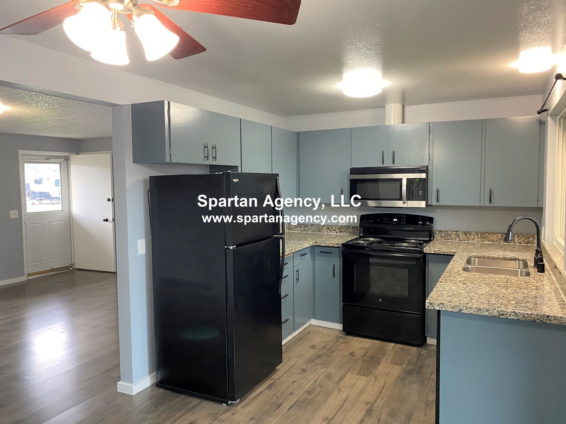 Kitchen with blue cabinets, granite countertops, black appliances, and light wood-look flooring.