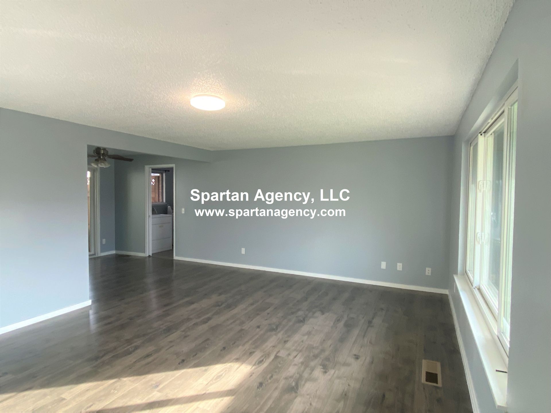 Empty living room with gray walls and flooring, a large window, and doorway.