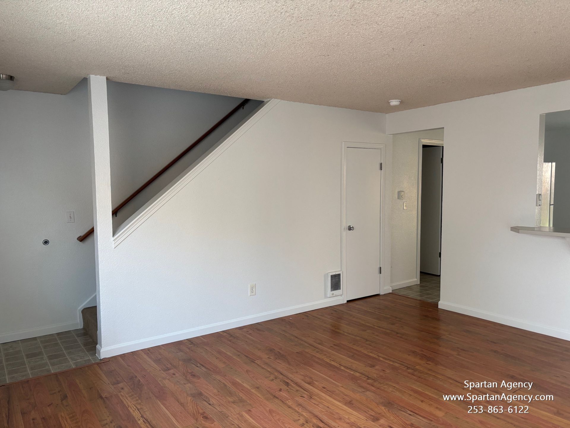 An empty living room with hardwood floors and white walls.