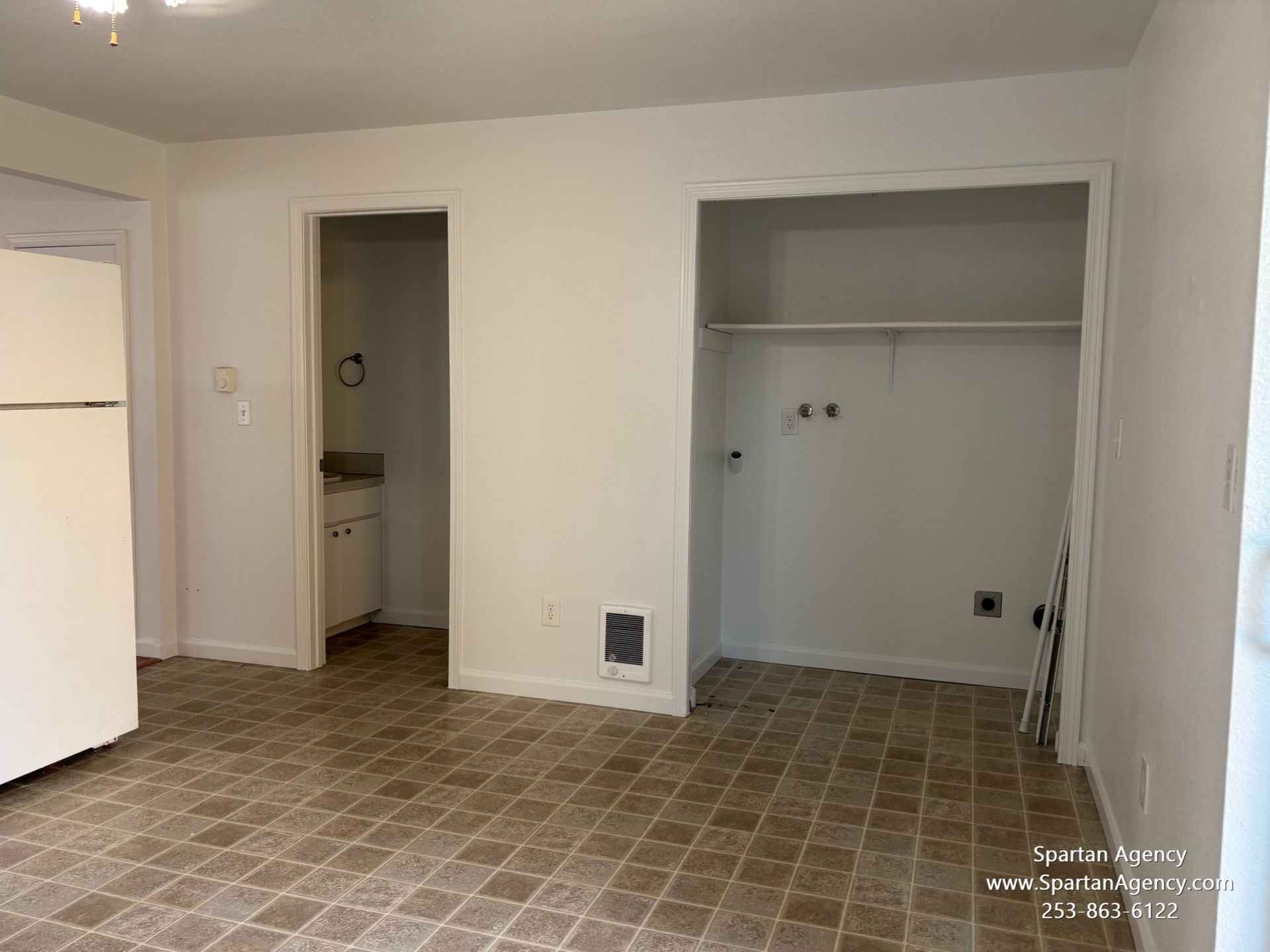 An empty room with a refrigerator and a closet.