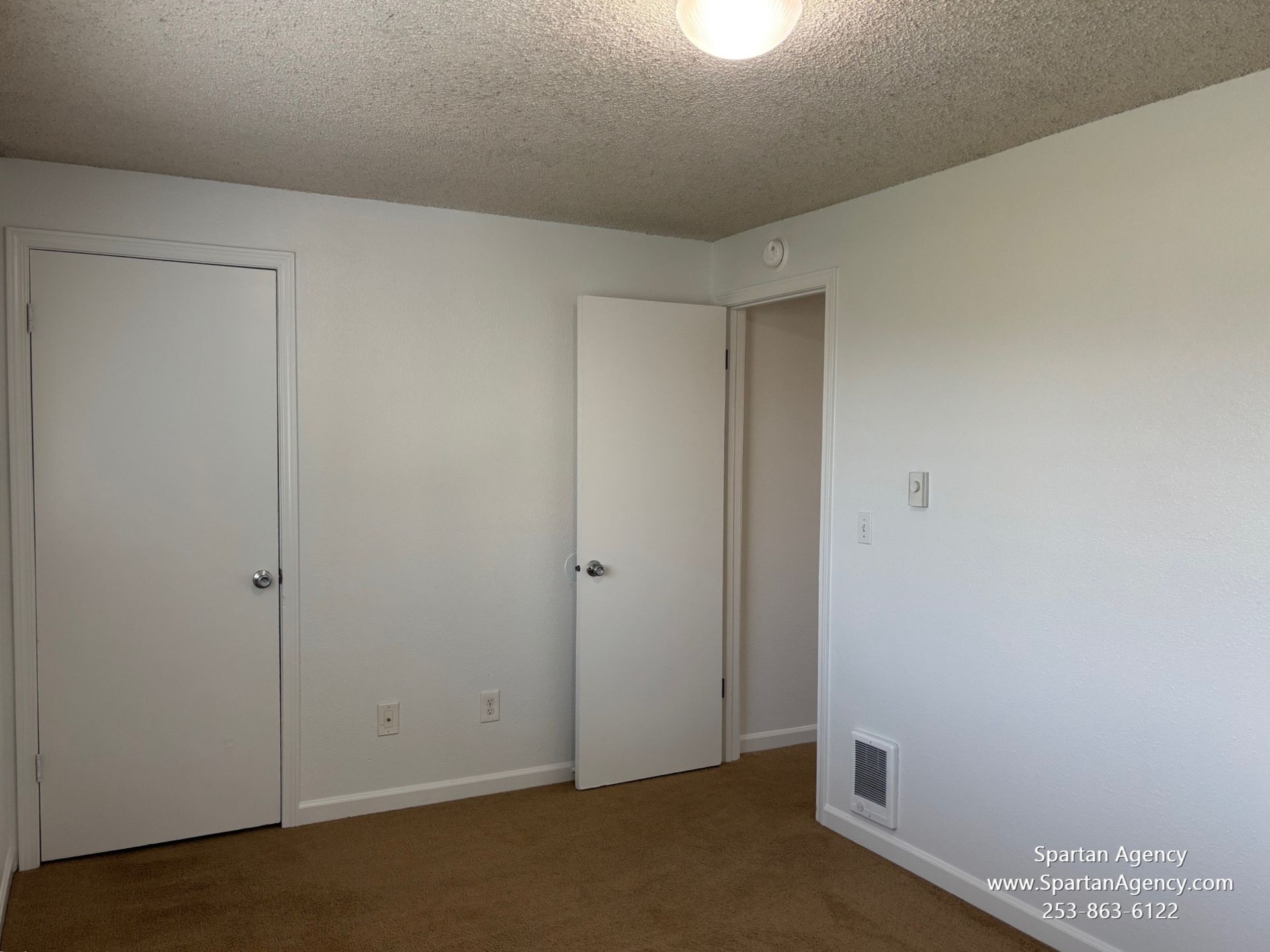An empty bedroom with white walls and brown carpet
