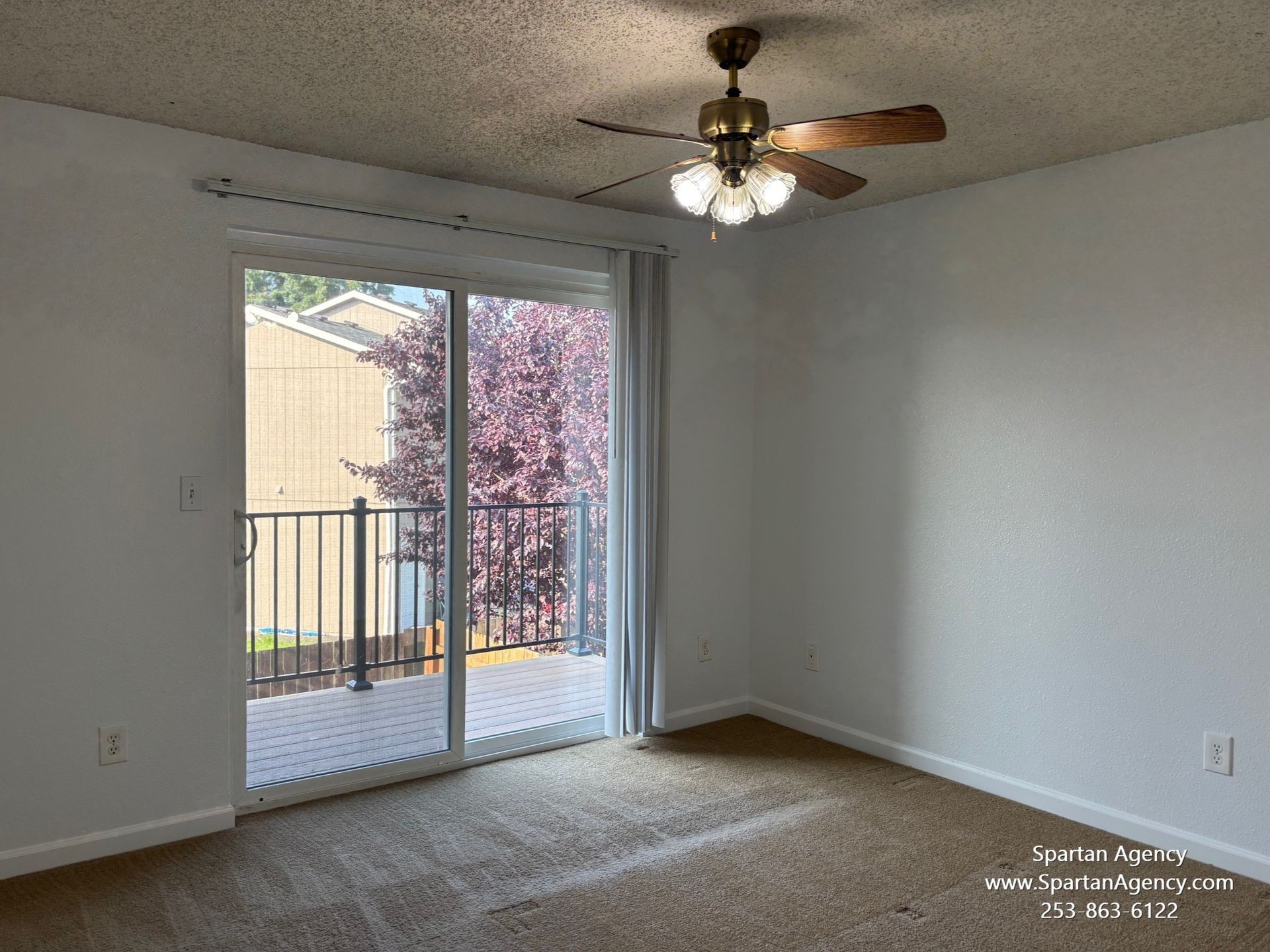 An empty room with a ceiling fan and sliding glass doors leading to a balcony.