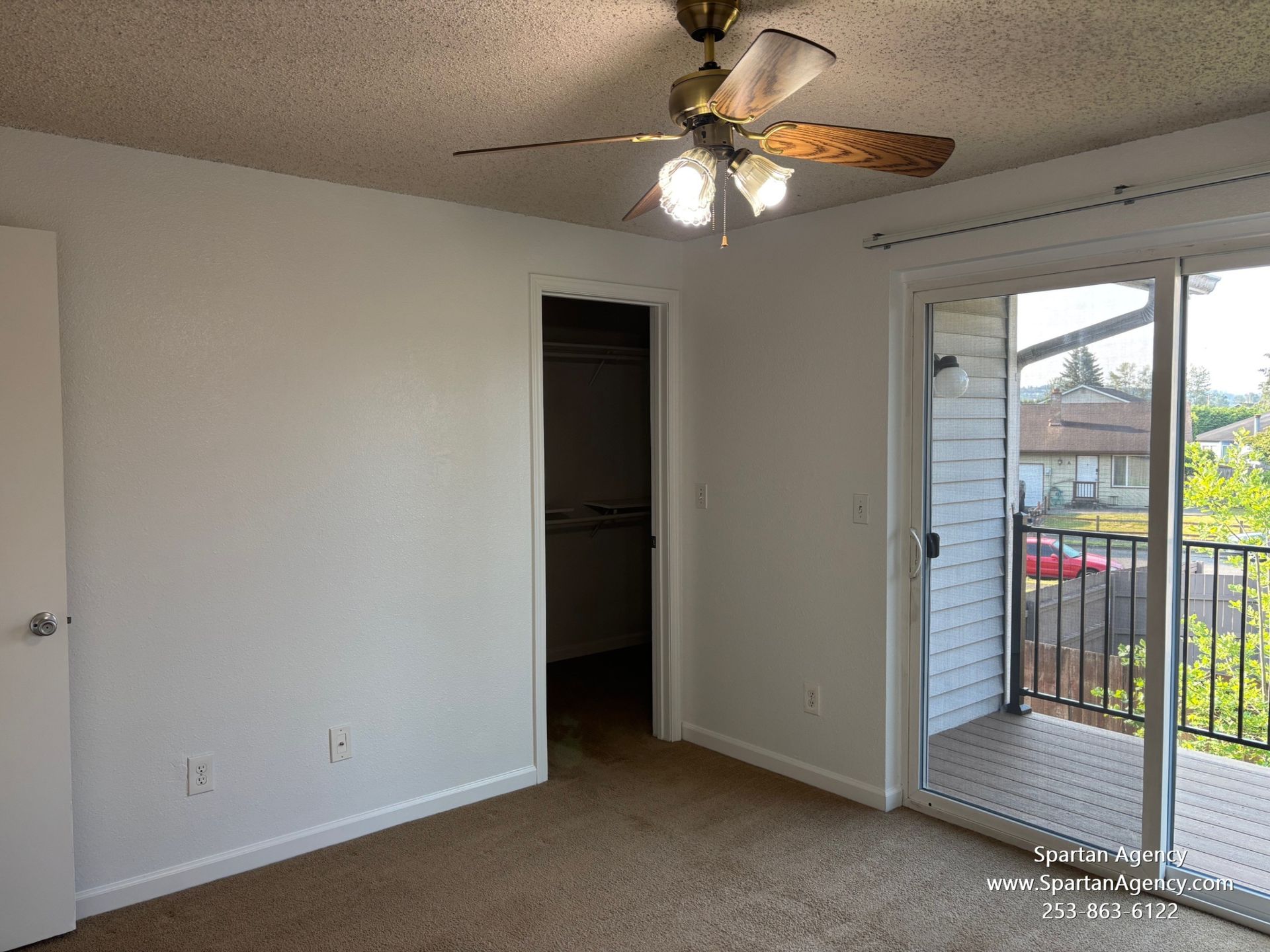 An empty bedroom with a ceiling fan and sliding glass doors