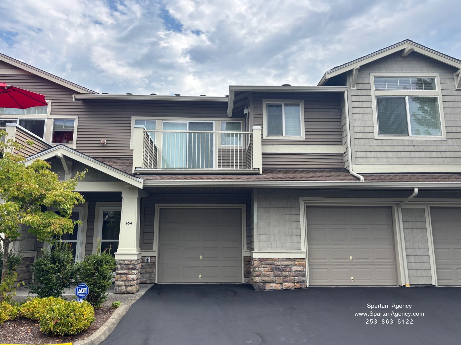 Townhouse with beige siding, tan garage doors, and a small balcony under cloudy skies.
