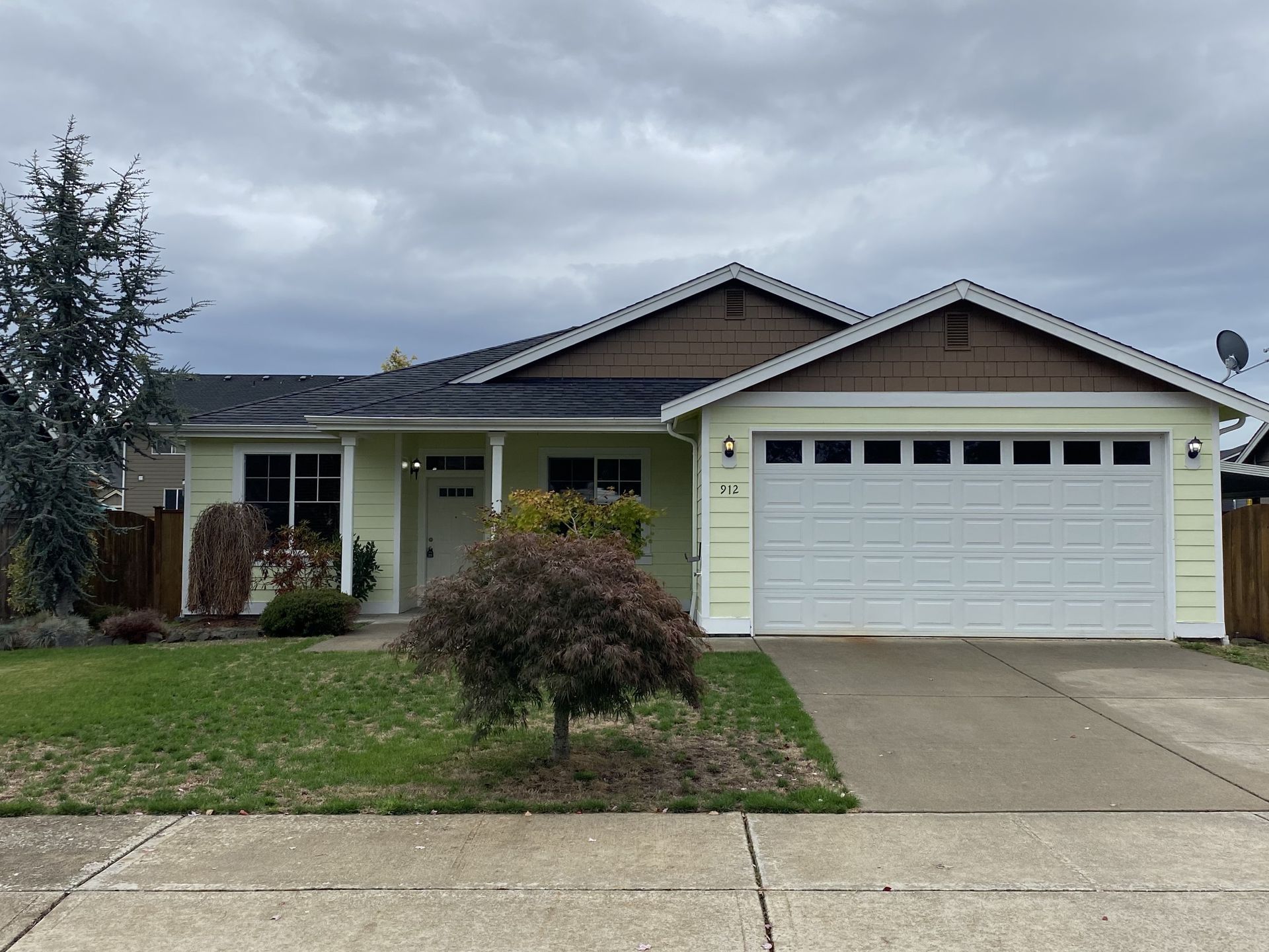 Light yellow house with white garage door and brown trim under a cloudy sky.