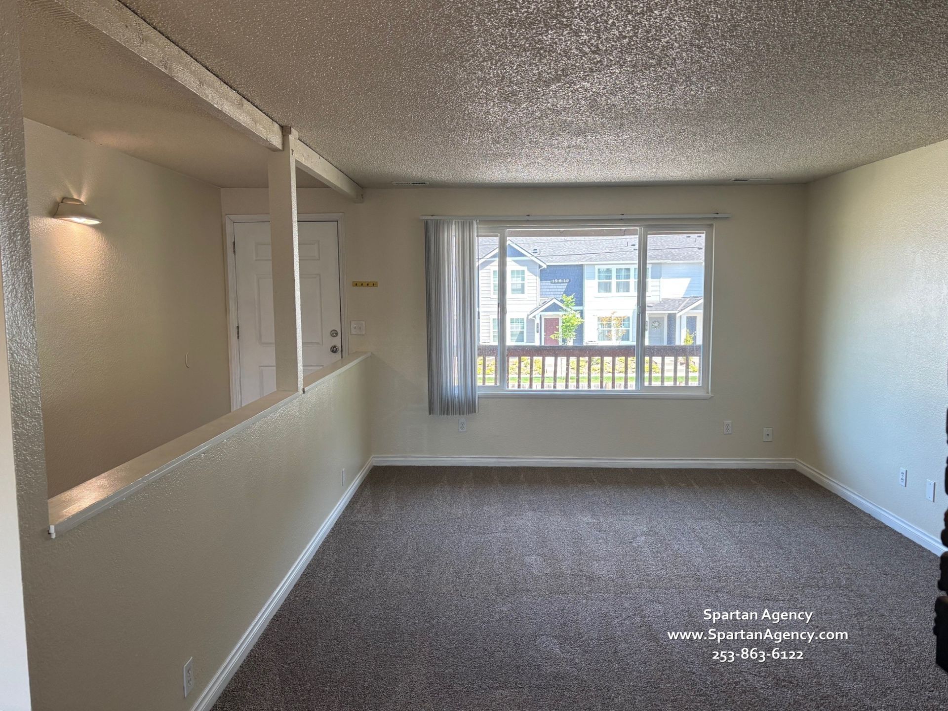 An empty living room with a large window and a carpeted floor