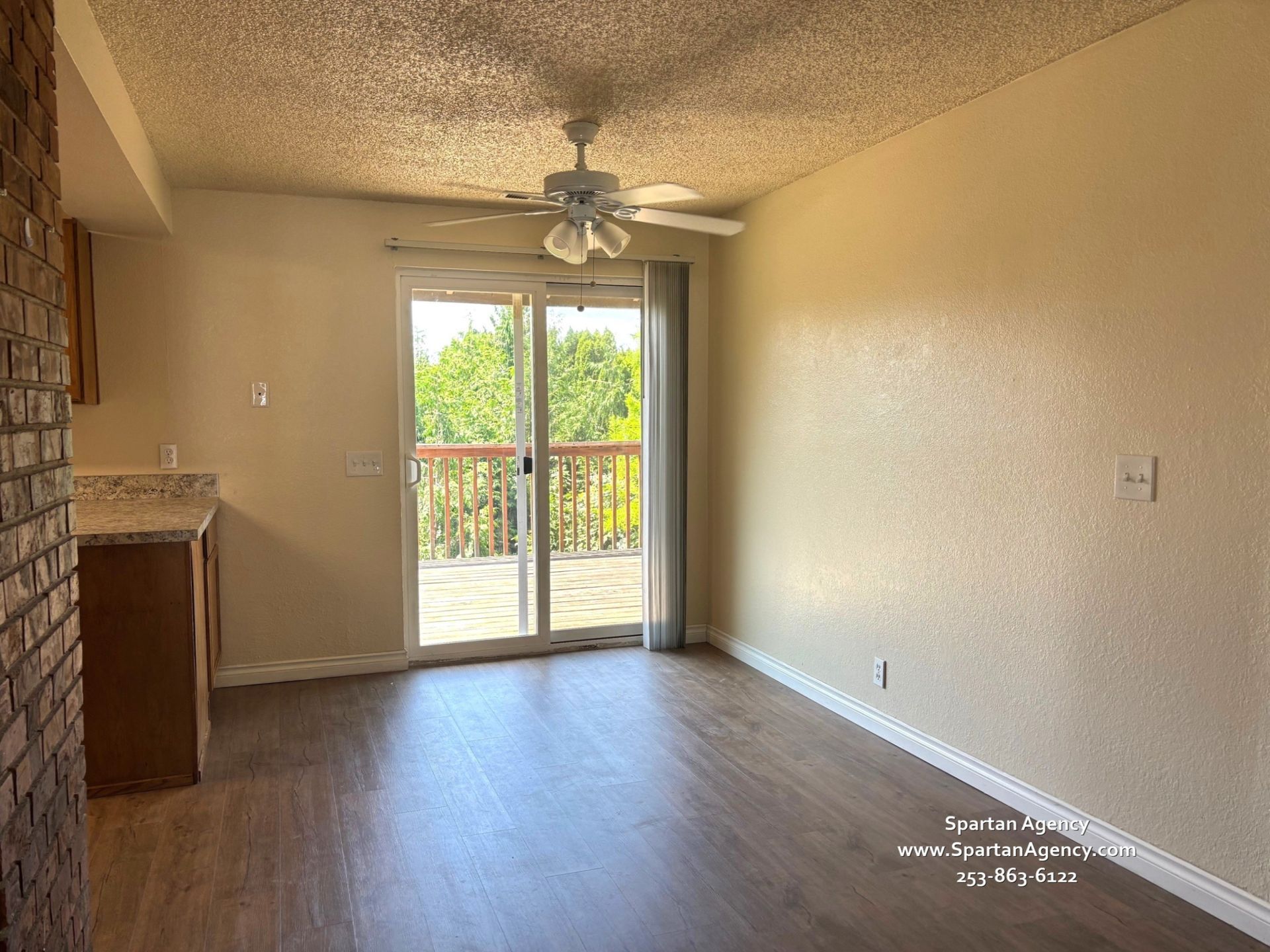 An empty living room with a ceiling fan and sliding glass doors leading to a balcony
