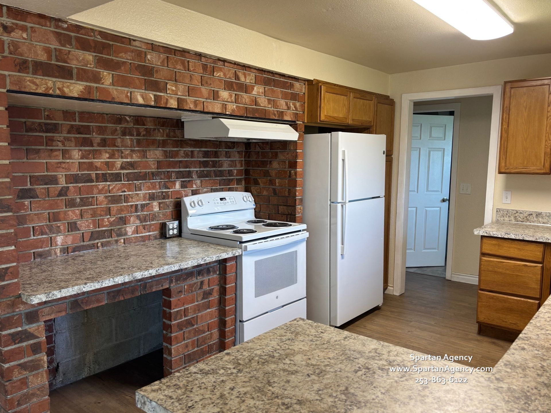 A kitchen with a stove, refrigerator, and brick wall