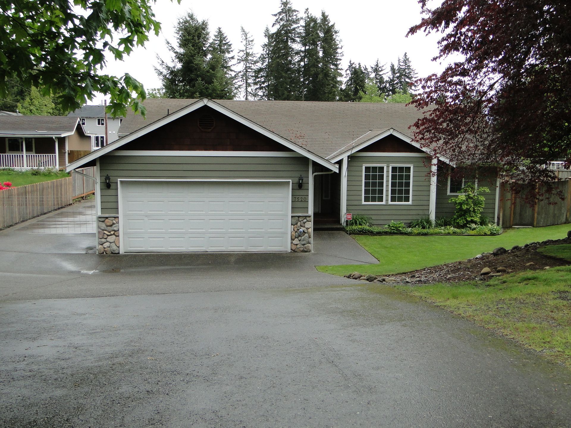 Green house with a two-car garage, gravel driveway, and small front yard.