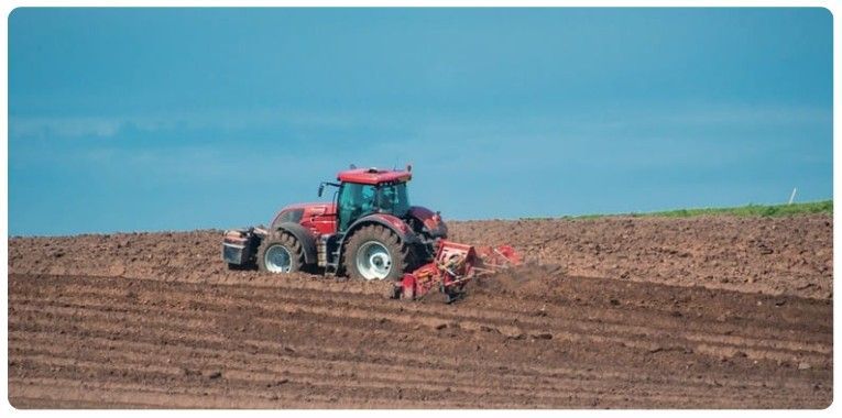 A red tractor plows a brown field under a clear blue sky.