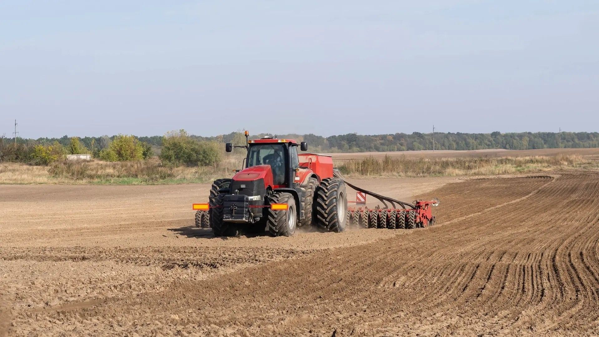 A red tractor is plowing a field on a sunny day.