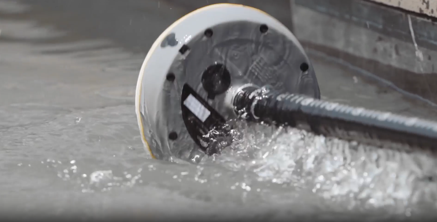 A rotating robotic device sprays water while moving along a concrete surface.