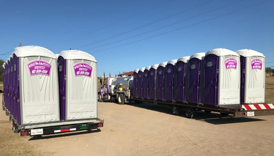 Two trailers carrying numerous purple portable toilets on a sunny day.