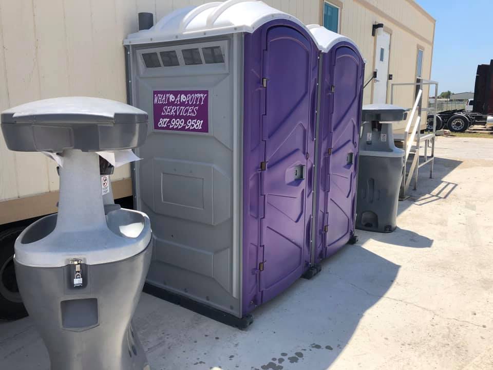 Two portable toilets, purple and gray, with a handwashing station on concrete.