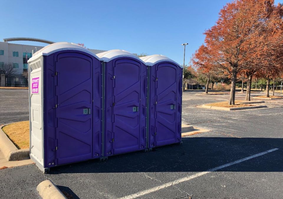 Three purple portable toilets in a parking lot on a sunny day.