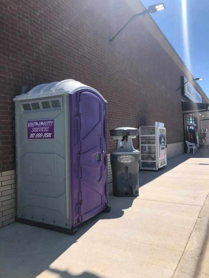 Gray and purple portable toilet, trash can, and vending machine outside a brick building.
