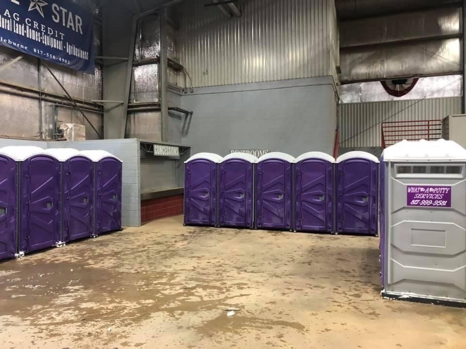 Indoor scene with rows of purple portable toilets in a building with metal walls.