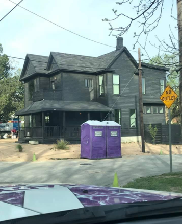 Black painted house with purple portable toilets on the front yard, 