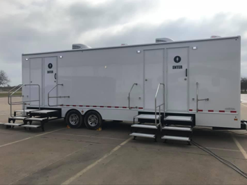 White portable restroom trailer with steps, on pavement.