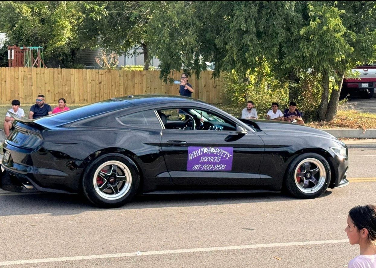 Black Ford Mustang with racing tires in a parade, people watching.