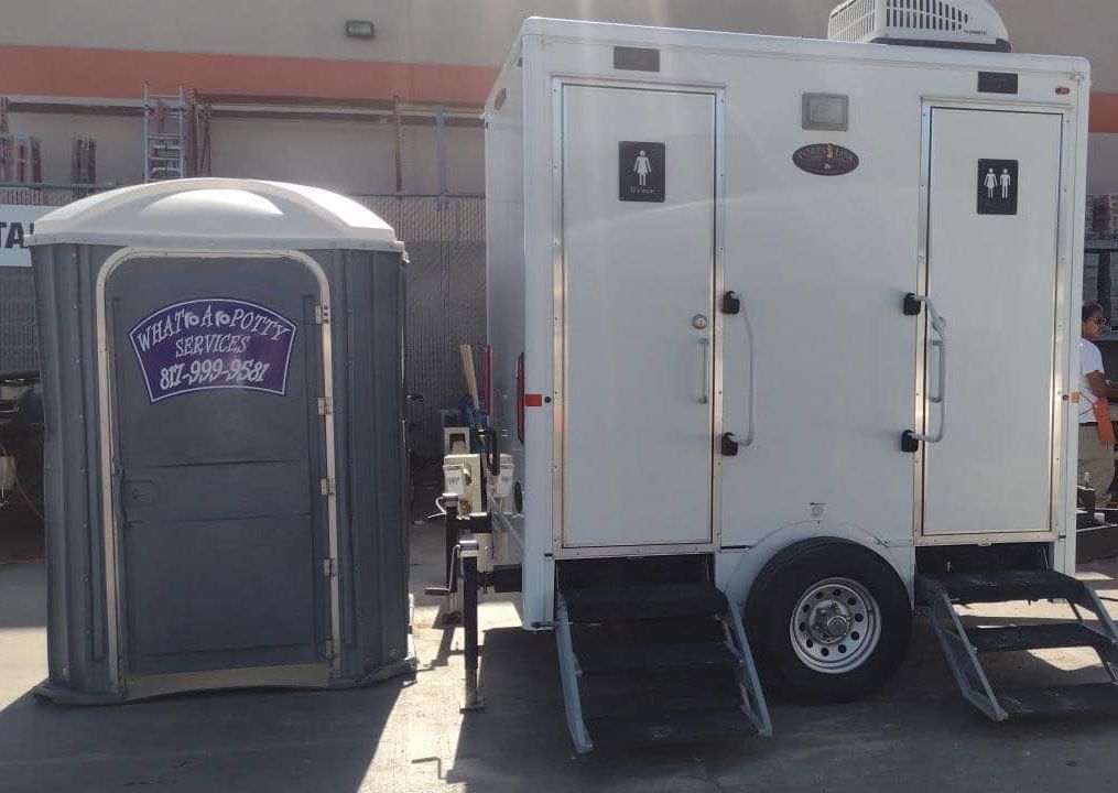 A portable toilet and a trailer are parked next to each other in a parking lot