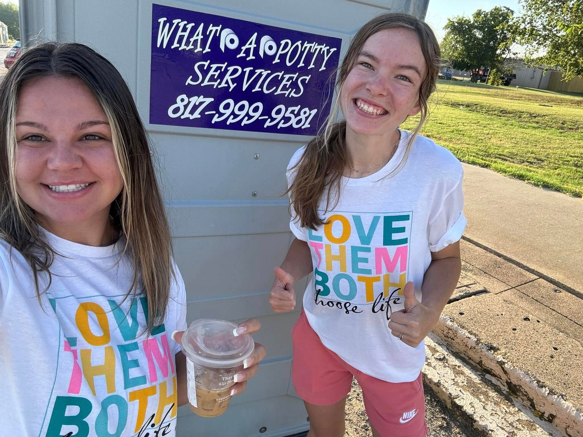 Two women smiling, giving thumbs-up. One holds a drink. They wear 