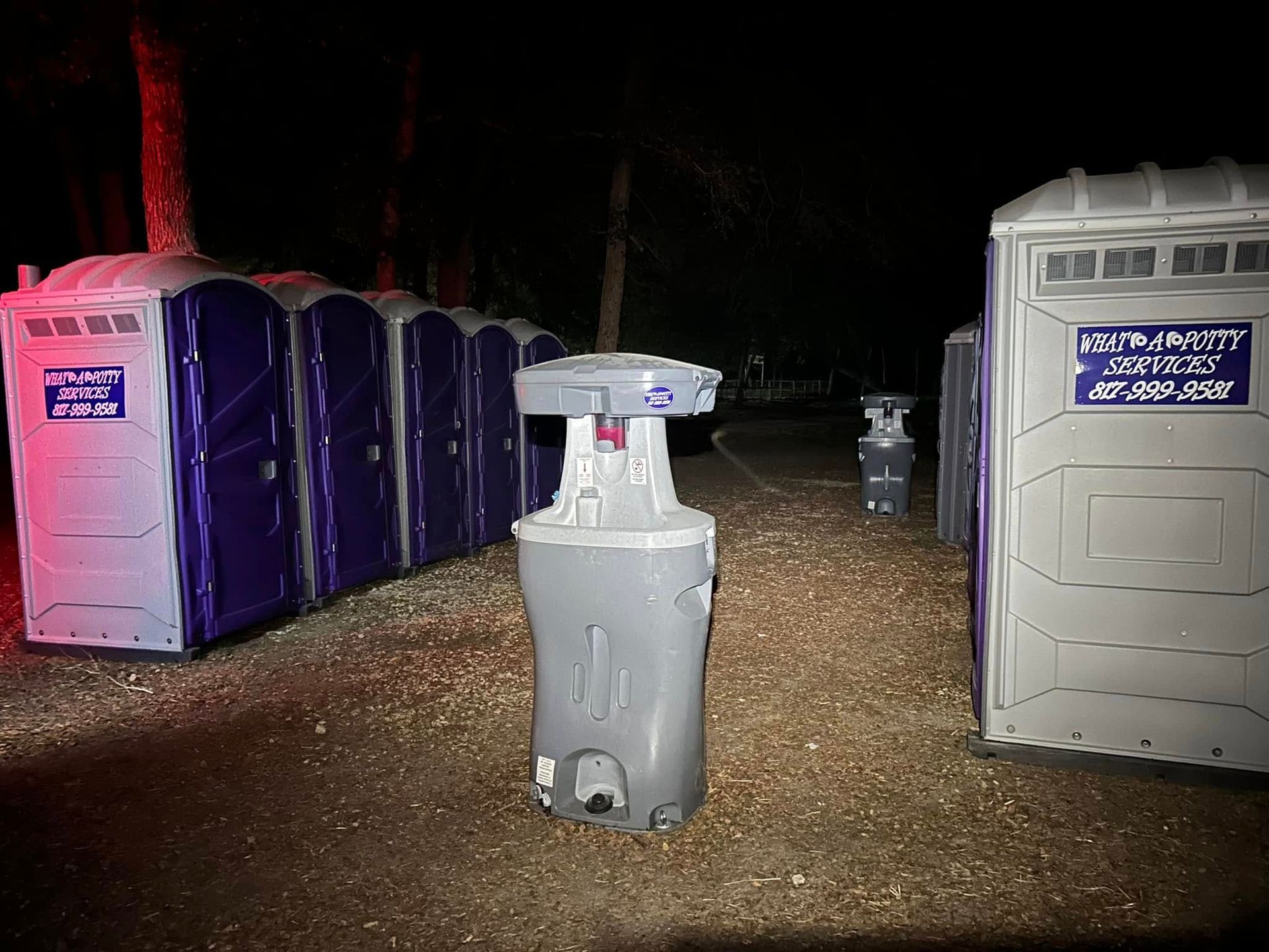 Portable toilets and handwashing station at night, outdoors. Gray and purple.