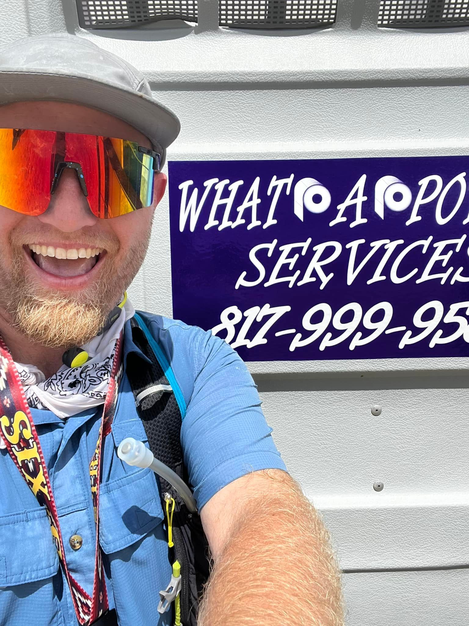 Man with sunglasses smiles, poses in front of a portable toilet service sign: 