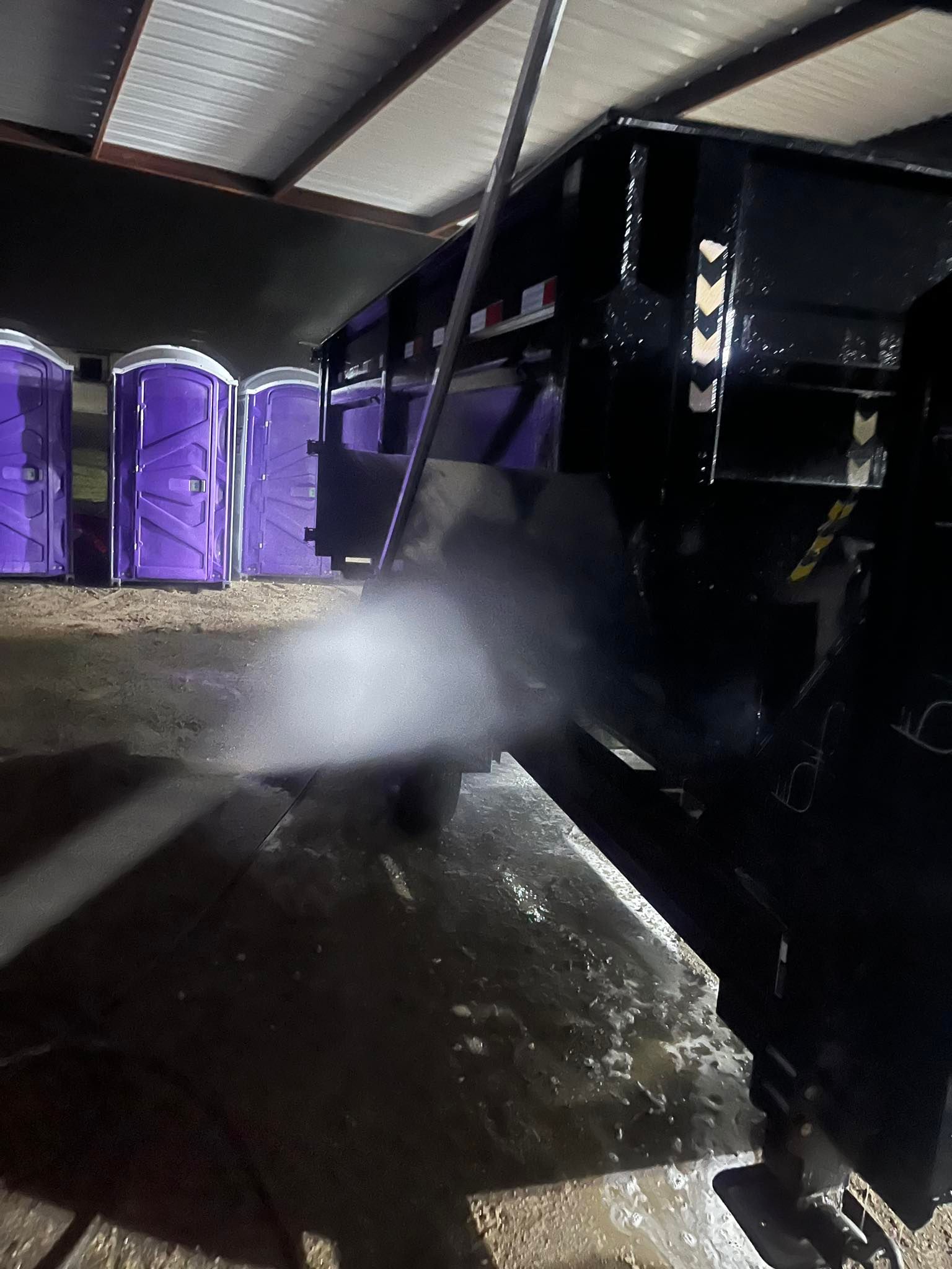A black trailer being pressure washed; purple portable toilets are in the background.