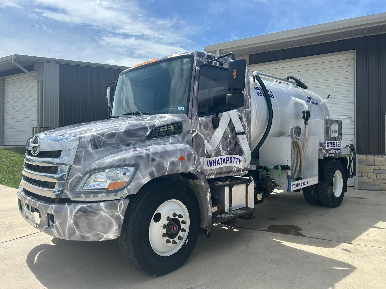Septic service truck with gray and blue wrap, parked in front of a building.
