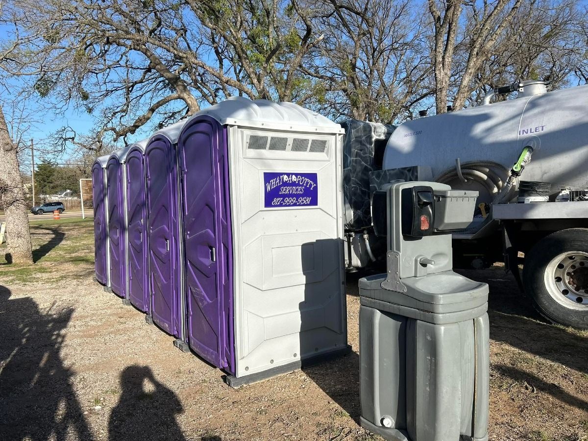 Portable toilets in a row, purple and white, next to a handwashing station and a tank truck.