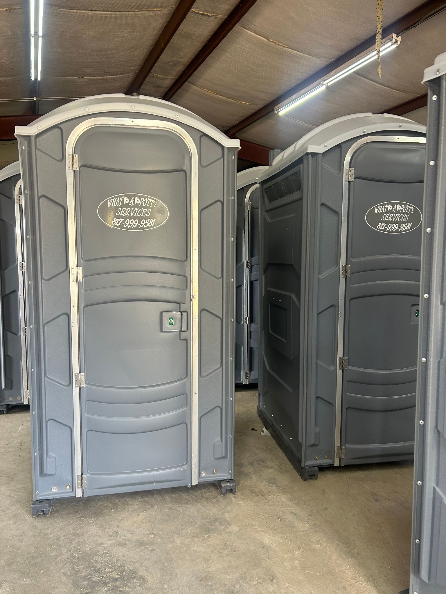 Several gray portable toilets, stored indoors.