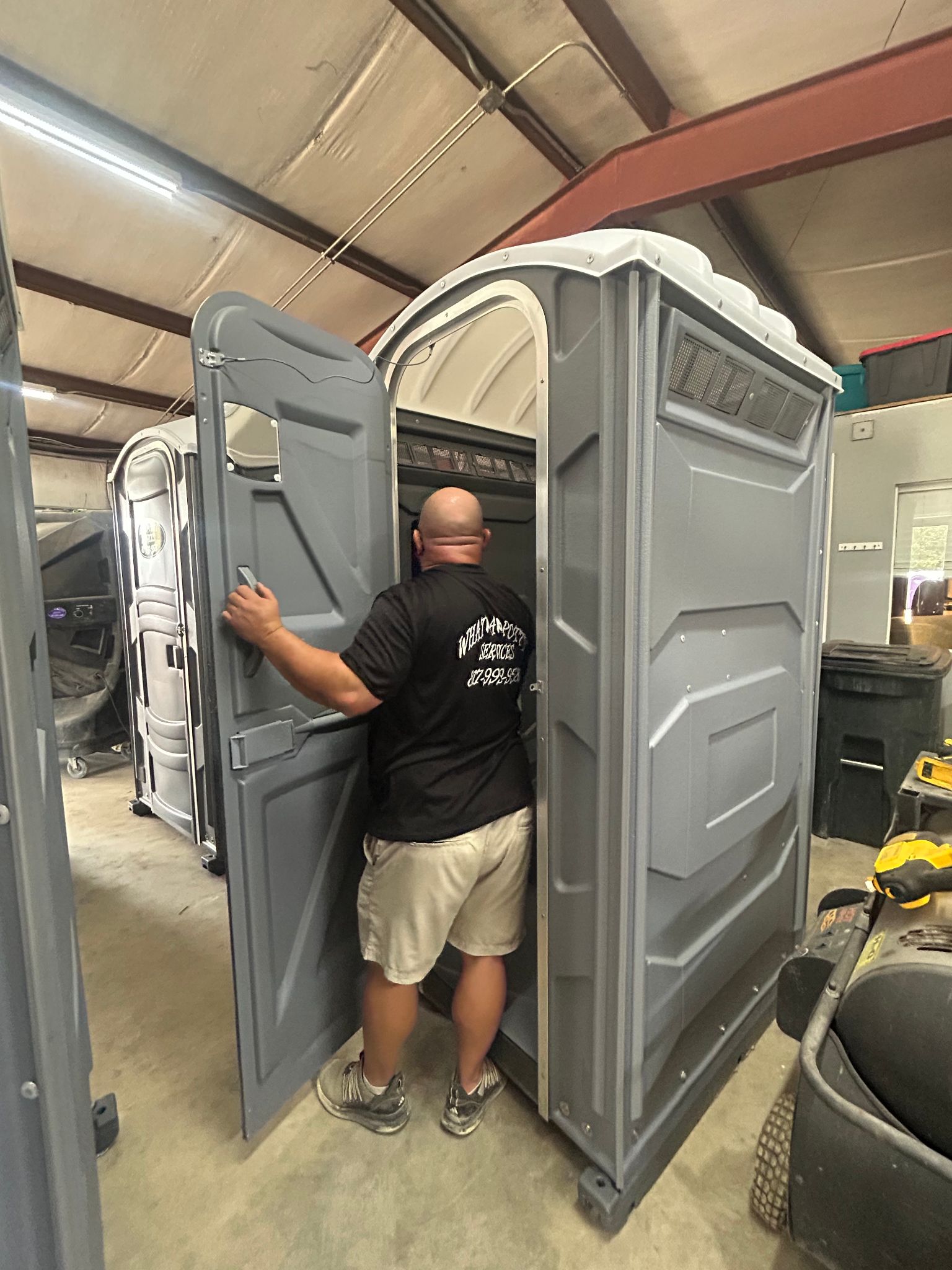 Man inspecting a gray portable toilet inside a warehouse.