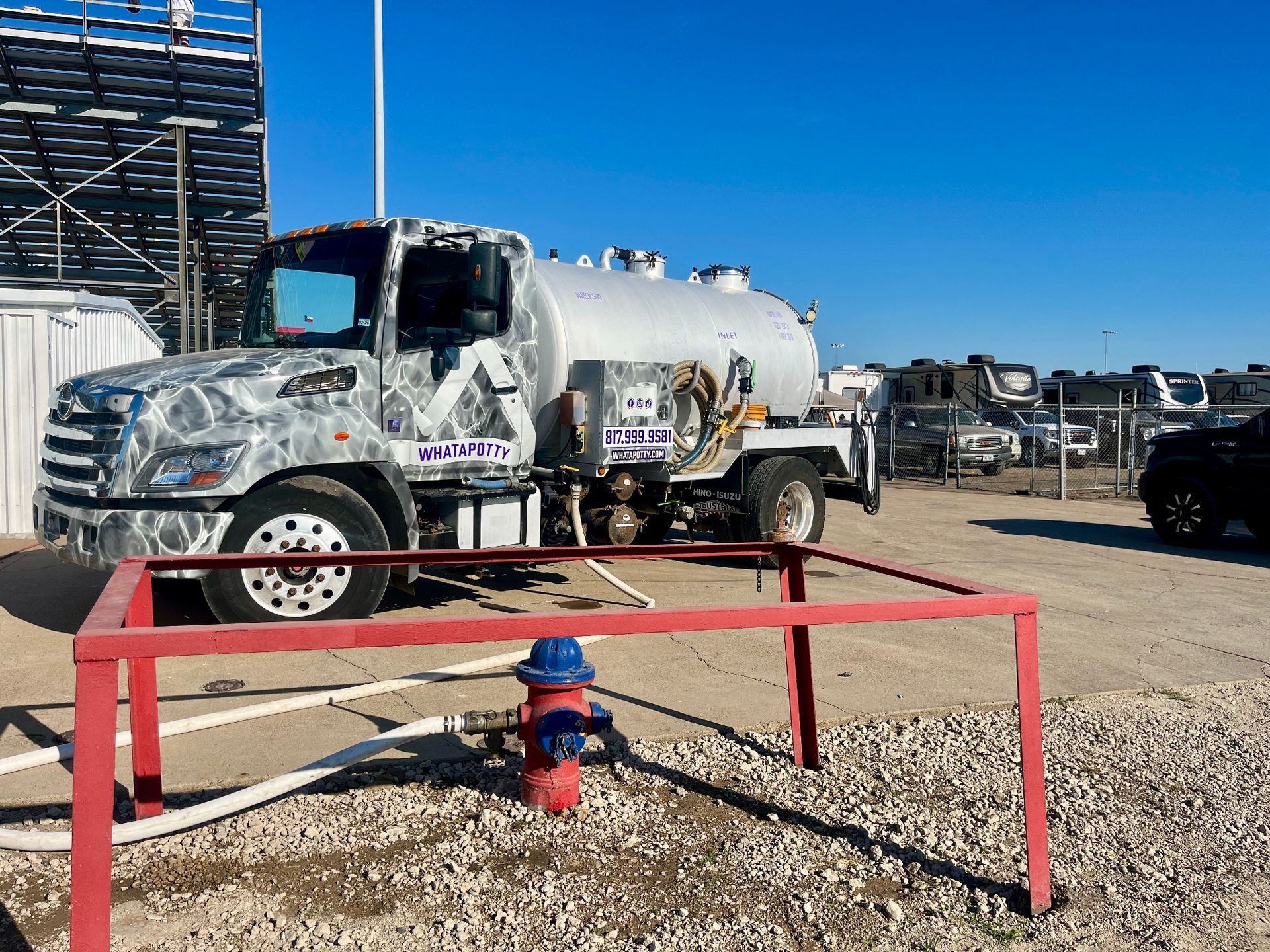Tanker truck near a fire hydrant; connected hose. Blue sky, outdoor setting.