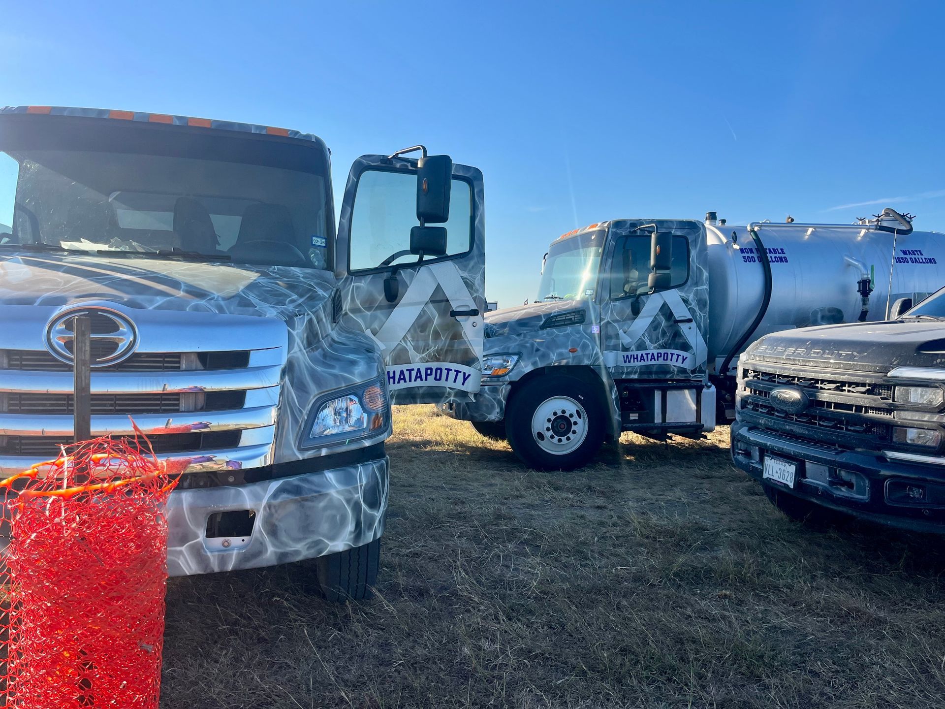 Three trucks with abstract grey and white designs parked in a field on a sunny day.