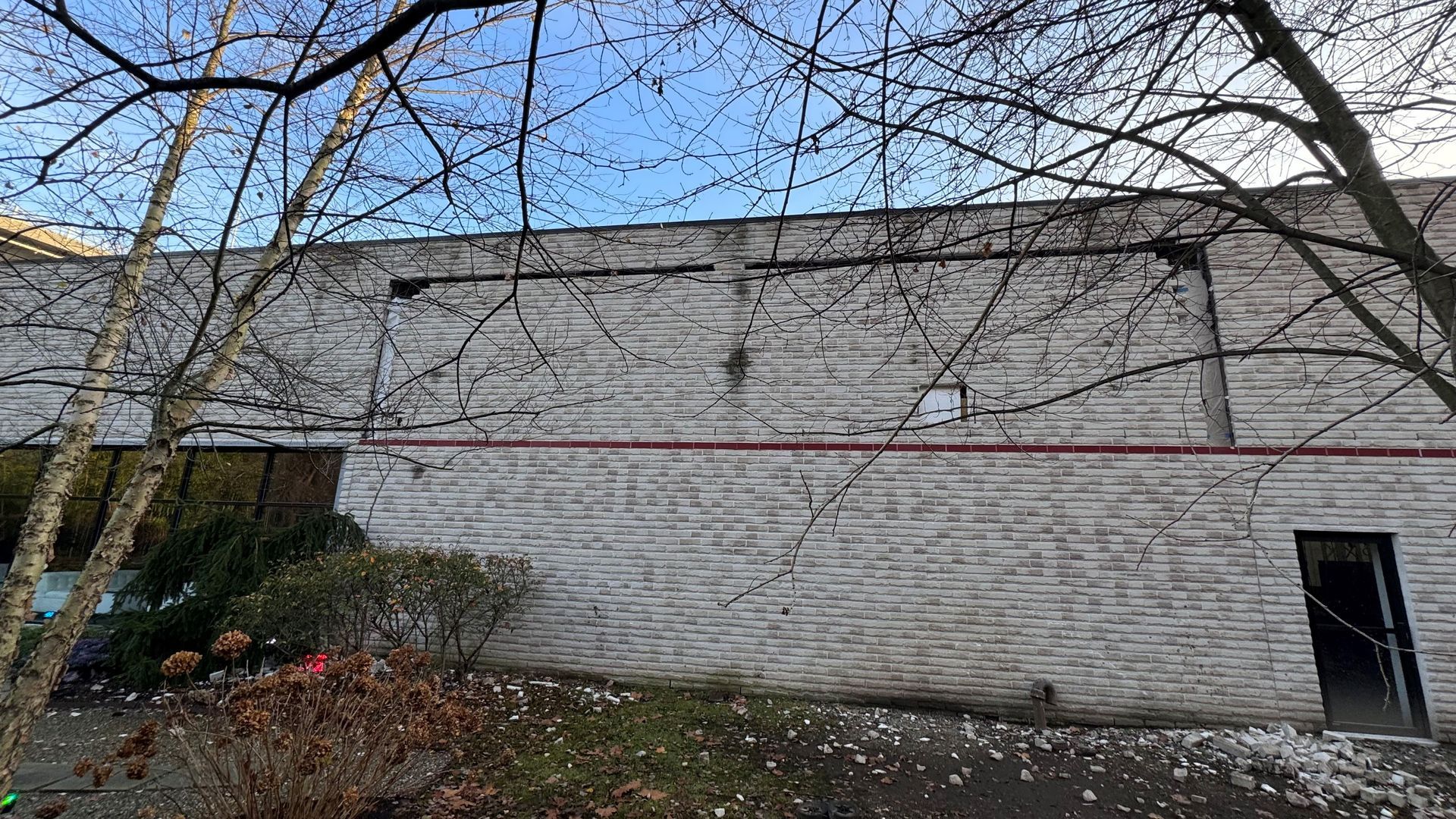 A white brick building with a door and trees in front of it.