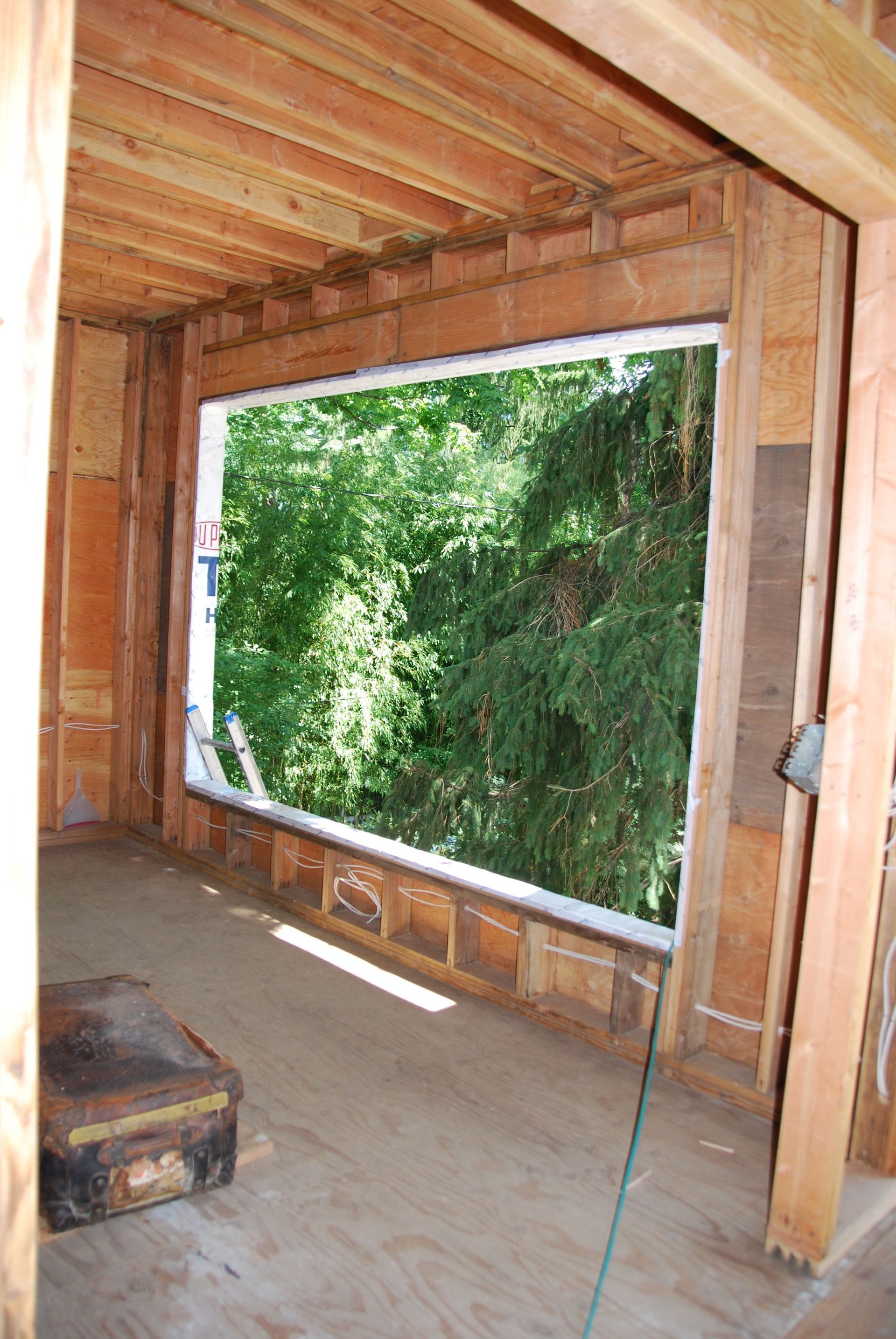 A large window in a wooden building with trees behind it.