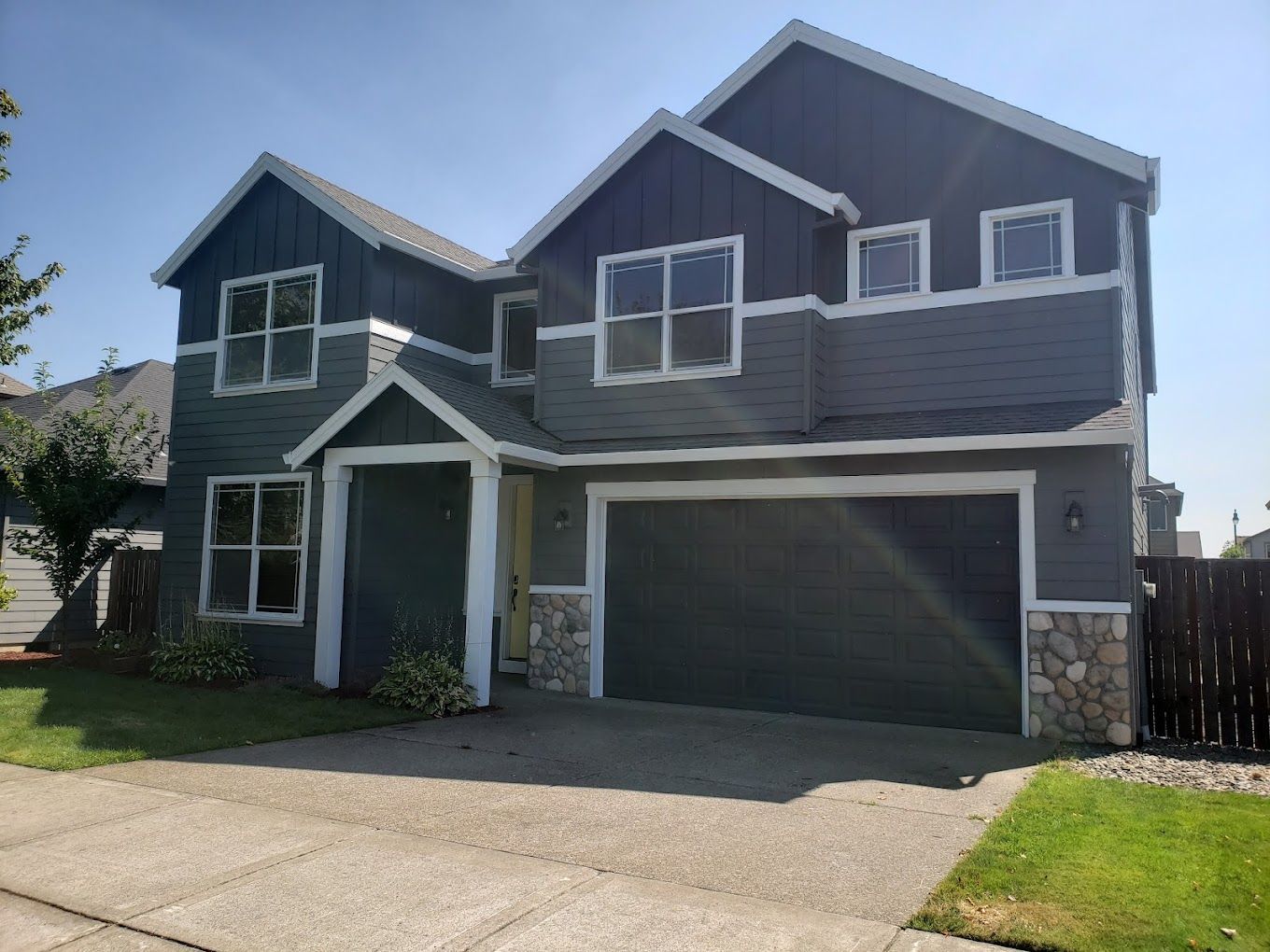 A large gray house with a garage and a fence in front of it.