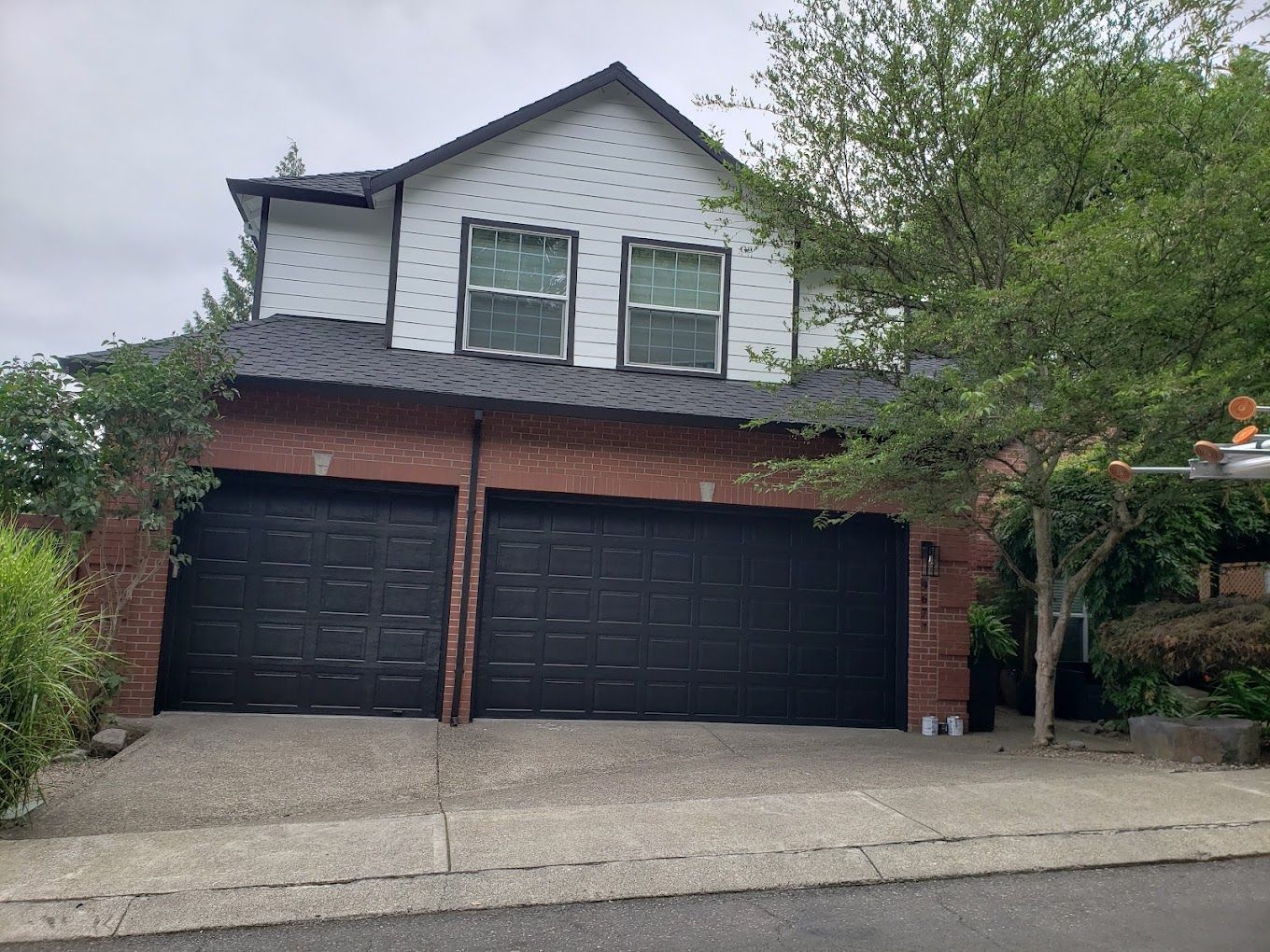 A white house with black garage doors and a black roof.