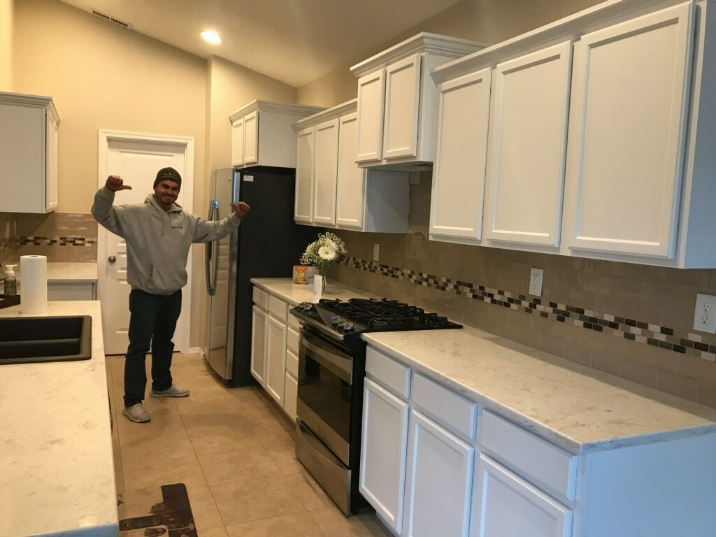 A man is standing in a kitchen with white cabinets and a black refrigerator.