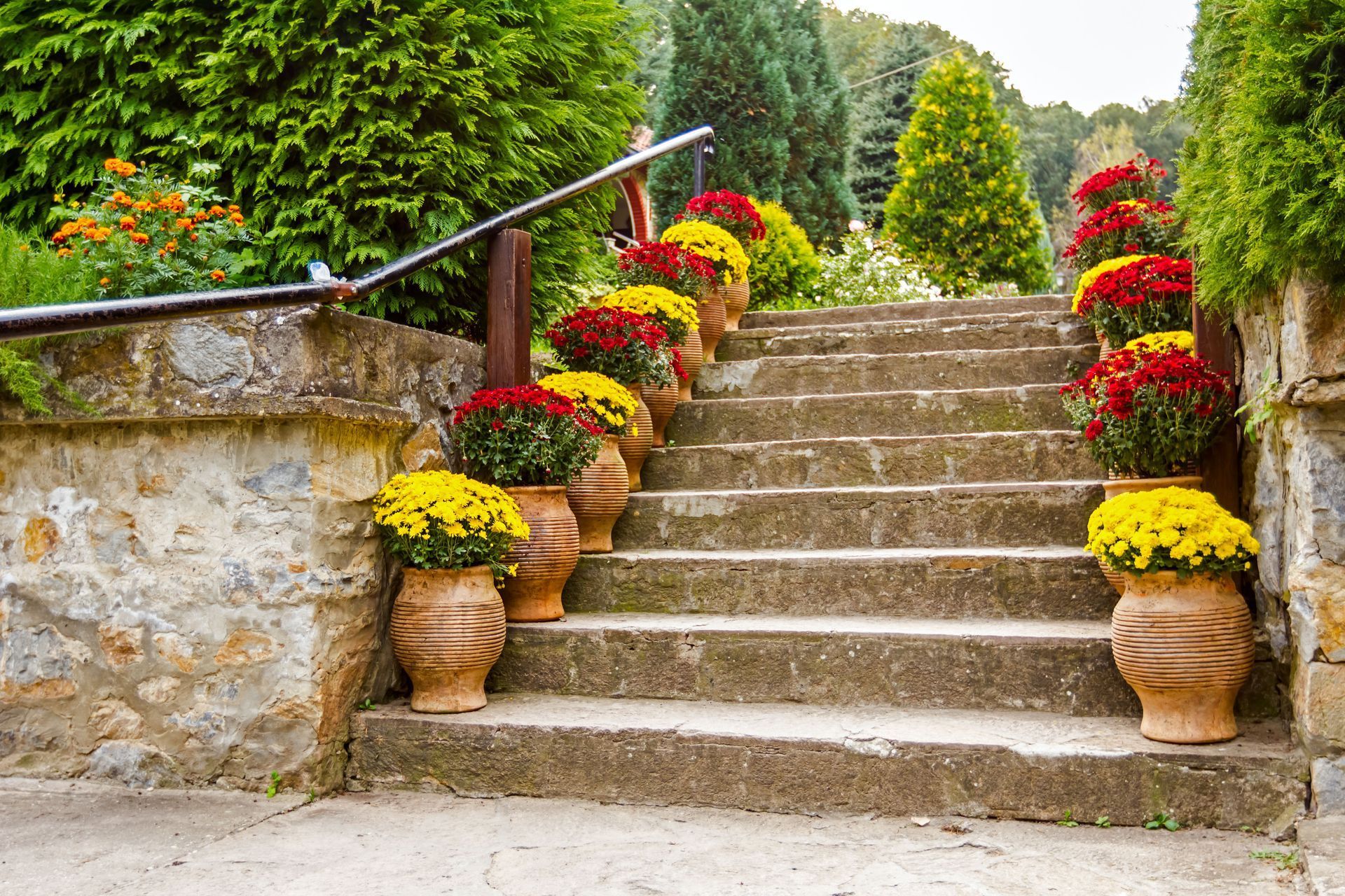 Stone garden staircase lined with colorful potted flowers and lush greenery