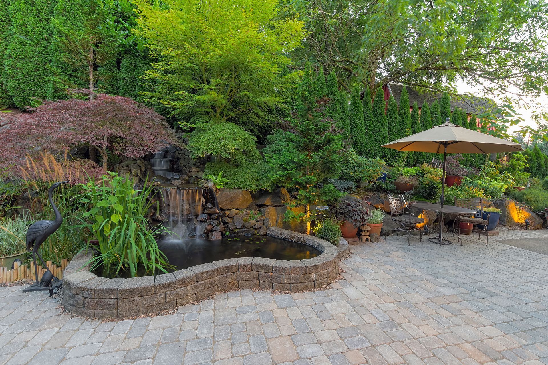 Garden patio with a small waterfall pond, potted plants, and a shaded seating area under an umbrella