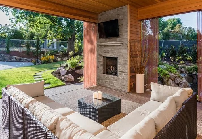 Covered patio with wicker seating around a fireplace, overlooking a landscaped backyard