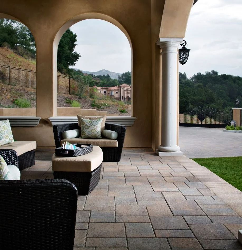 Covered patio with wicker seating and stone tile floor overlooking a landscaped hillside view