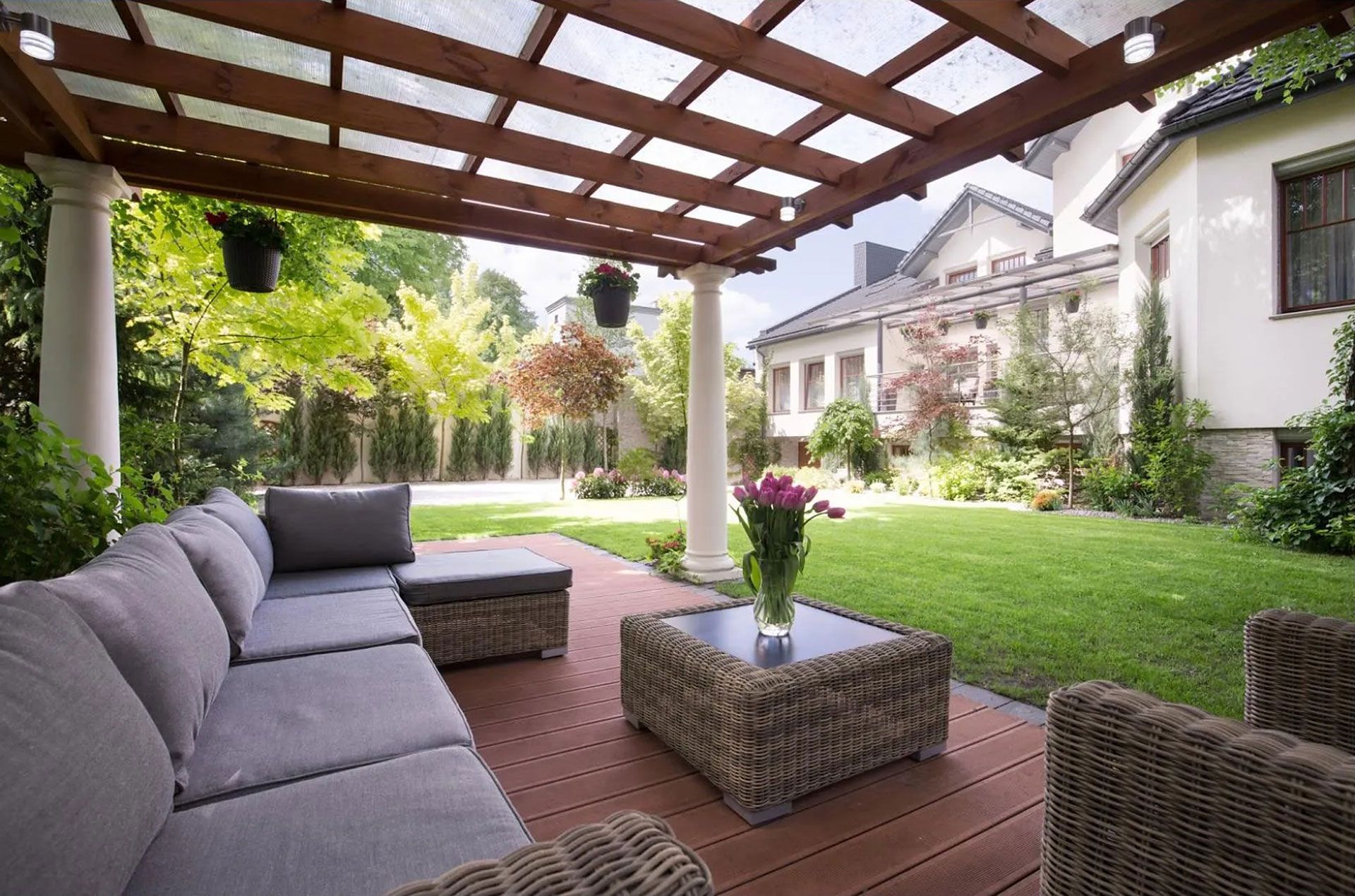 Covered patio with gray sectional seating, wicker tables, and a green backyard lawn