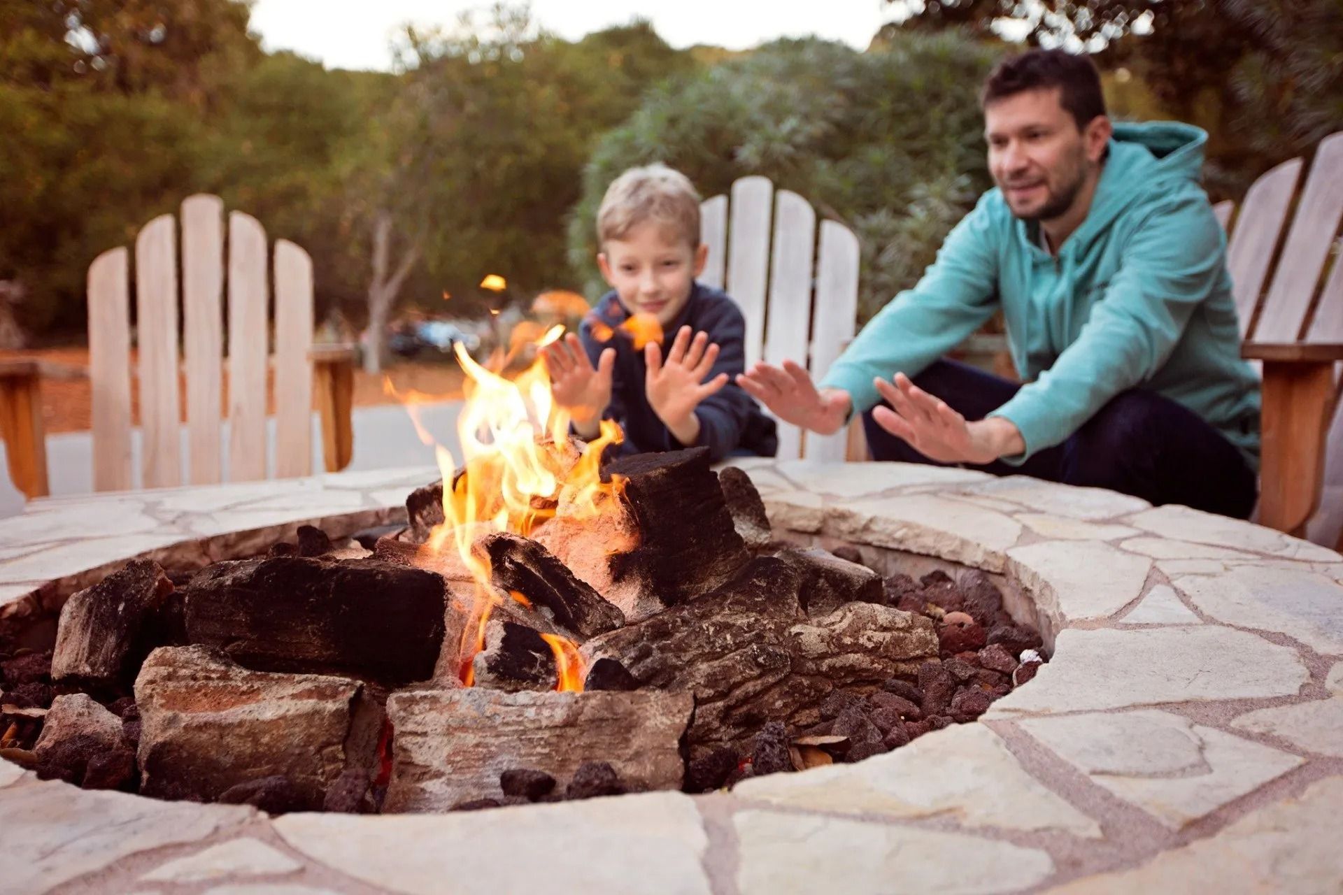 Adult and child warming hands by a backyard fire pit at dusk