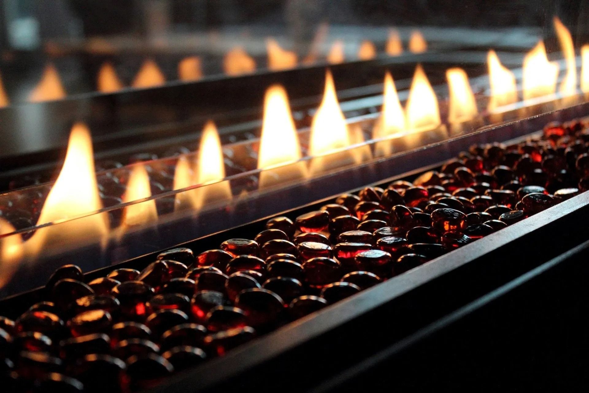 Row of bright flames over red embers in a dark metal fire pit