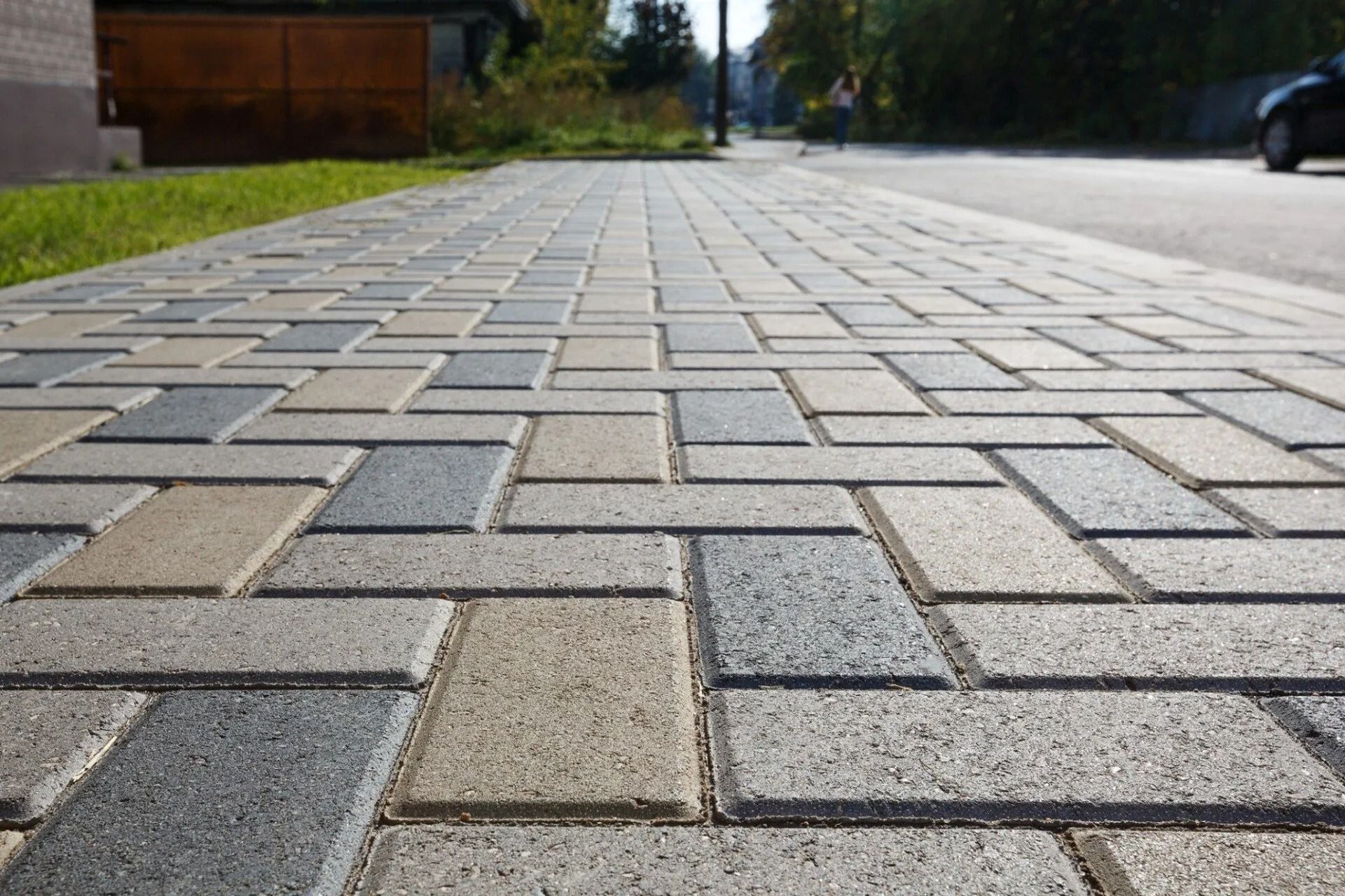 Low-angle view of a paved brick sidewalk beside a road and grassy verge